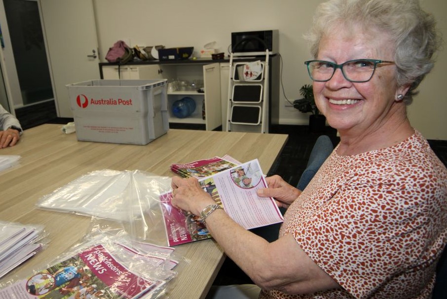 A lady smiles over her shoulder and packs a newsletter in a bag.
